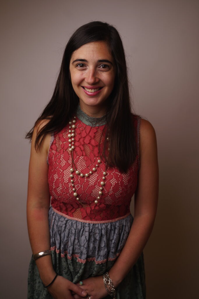 A color photograph headshot of a young woman with long dark hair in a dress with a dark pink lace sleeveless top and a light green skirt.