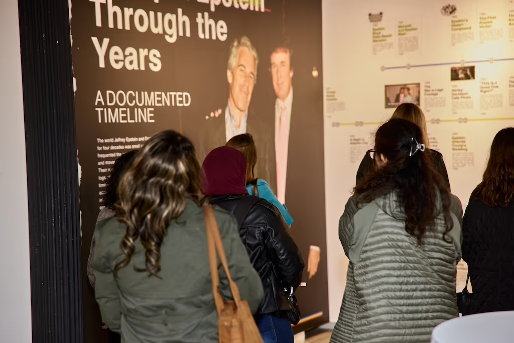 A photo of women seen from behind looking at a timeline of Jeffrey Epstein and Donald Trump's friendship, and the different allegations of sexual harassment and assault against both men, and Epstein's known sex trafficking operations. 