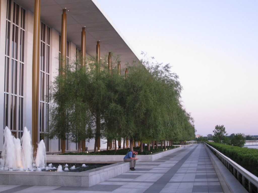 A photo of the Kennedy Center, seen from a side view with its gold columns, weeping willows, and fountains.