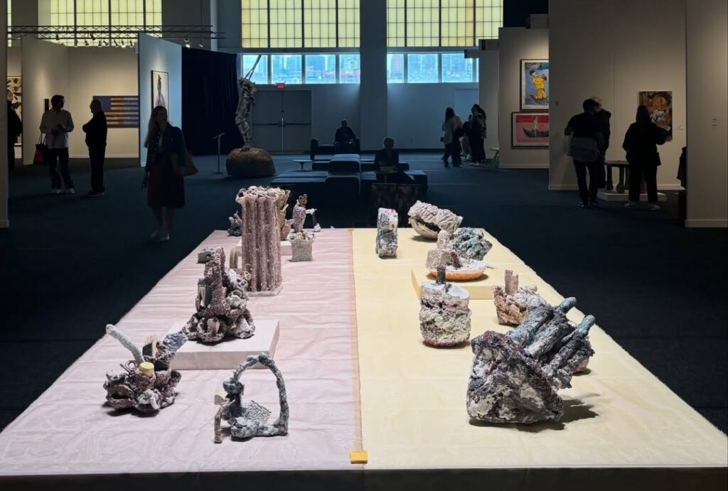 A photo of two rows of ceramic sculptures on display on a low plinth in an art fair. 
