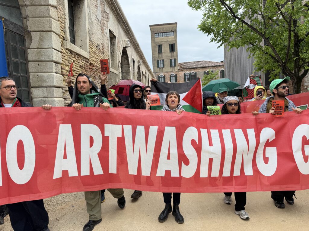 Current image: A photo of a group of protesters carrying a large red banner reading "artwashing."