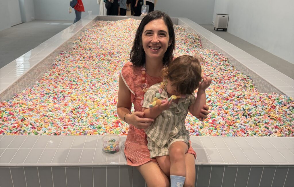 A woman and a toddler sit on the edge of a large pit of colorful plastic beads.