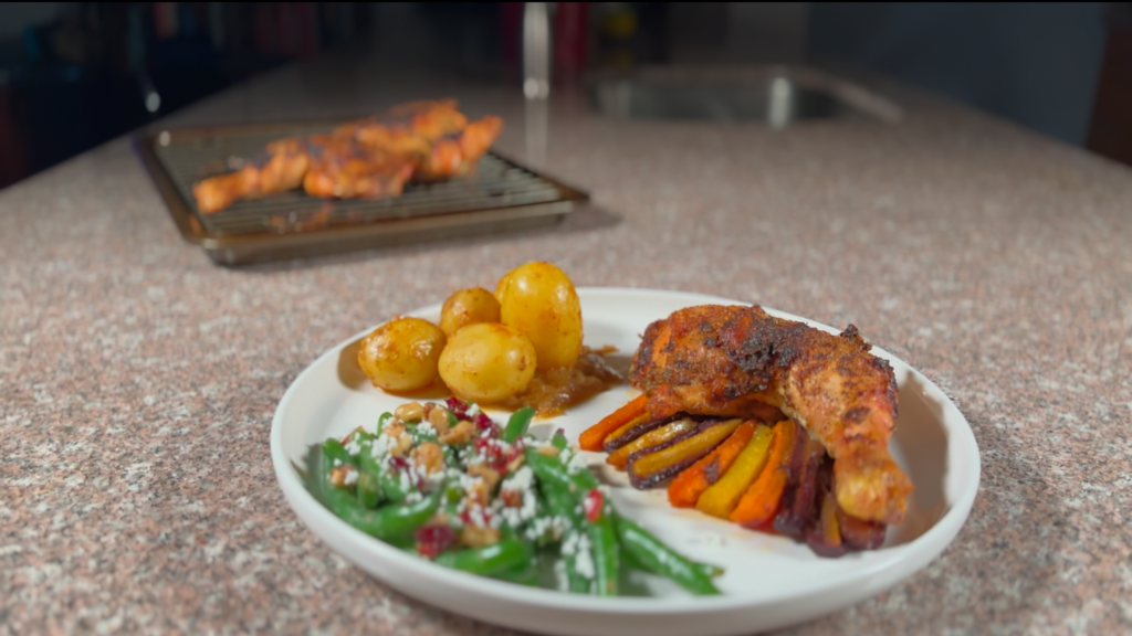 A photo of a plate of food on a granite counter, with green beans, carrots, potatoes, and roast chicken. 