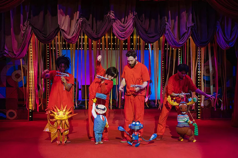 A photo of puppeteers performing on a red stage.