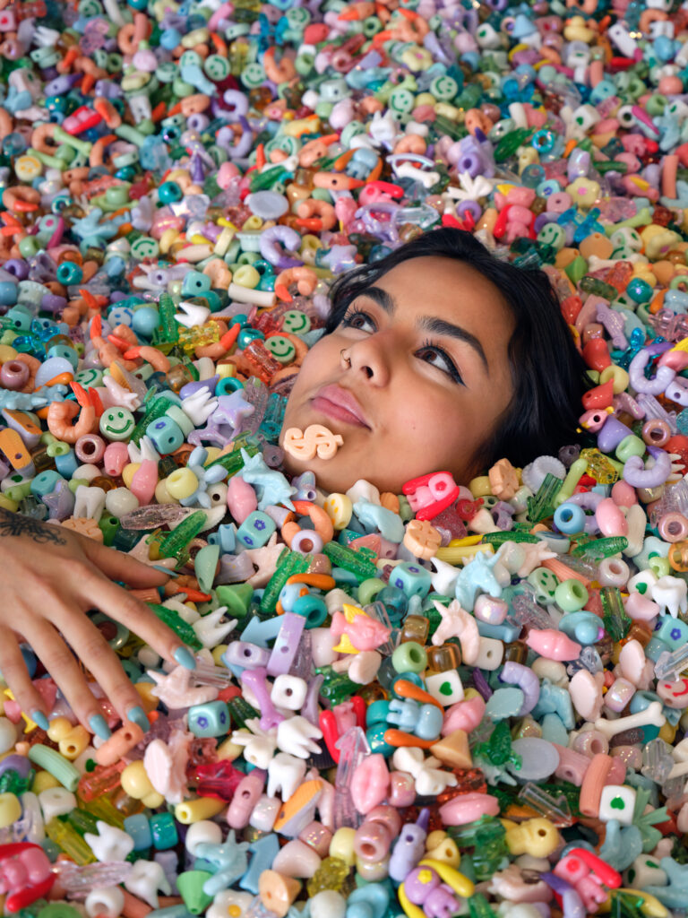A woman's face emerges amid a seemingly endless pit of plastic beads.